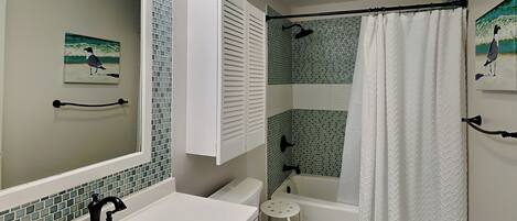 Et badeværelse med en hvid vask, toilet og badekar. Der er et brusebord og en lille skammel.
