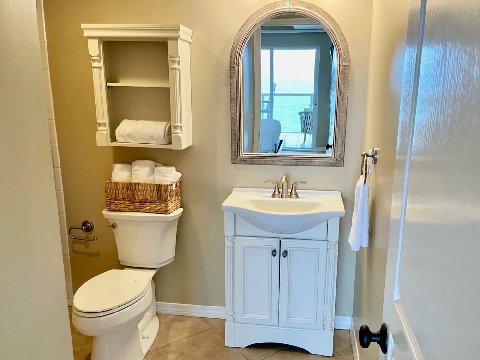 A bathroom with a toilet, a sink, a mirror, and a basket of towels.
