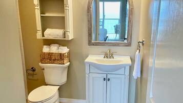 A bathroom with a toilet, a sink, a mirror, and a basket of towels.
