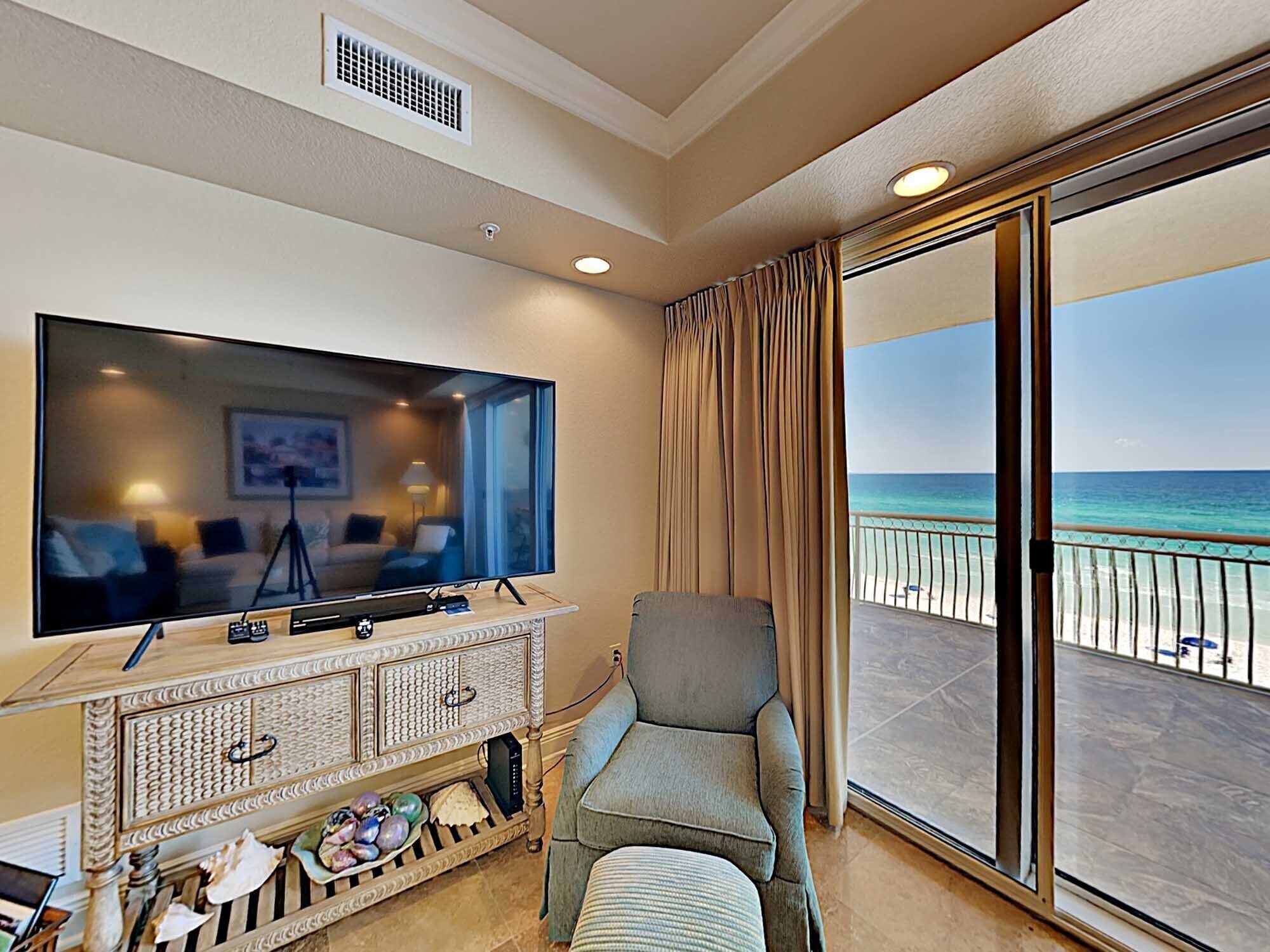 Un balcón con vista al océano, un televisor y una zona de estar con una mesa y objetos decorativos.