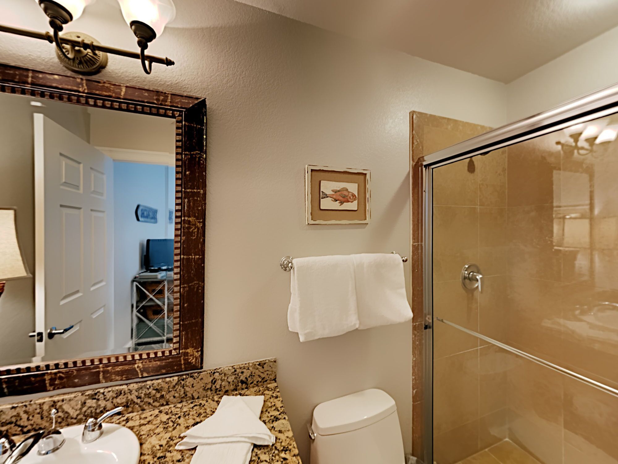 A bathroom with a large mirror, granite countertop, two sinks, a toilet, and a glass shower enclosure.