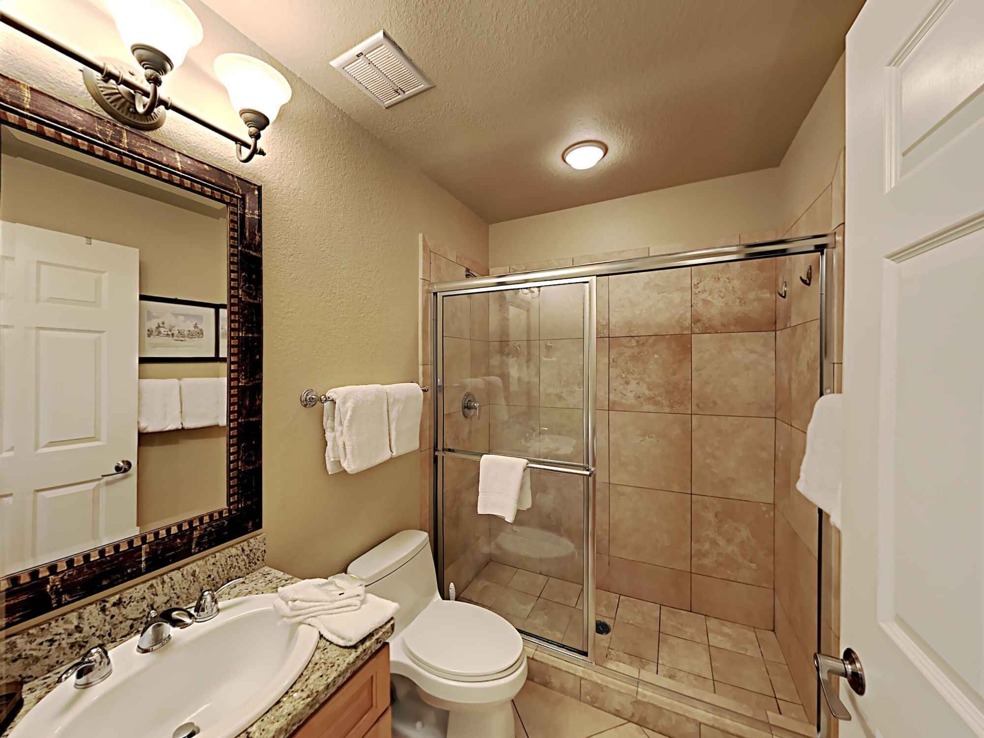 A bathroom with a glass-enclosed shower, a sink with a mirror, and a toilet.