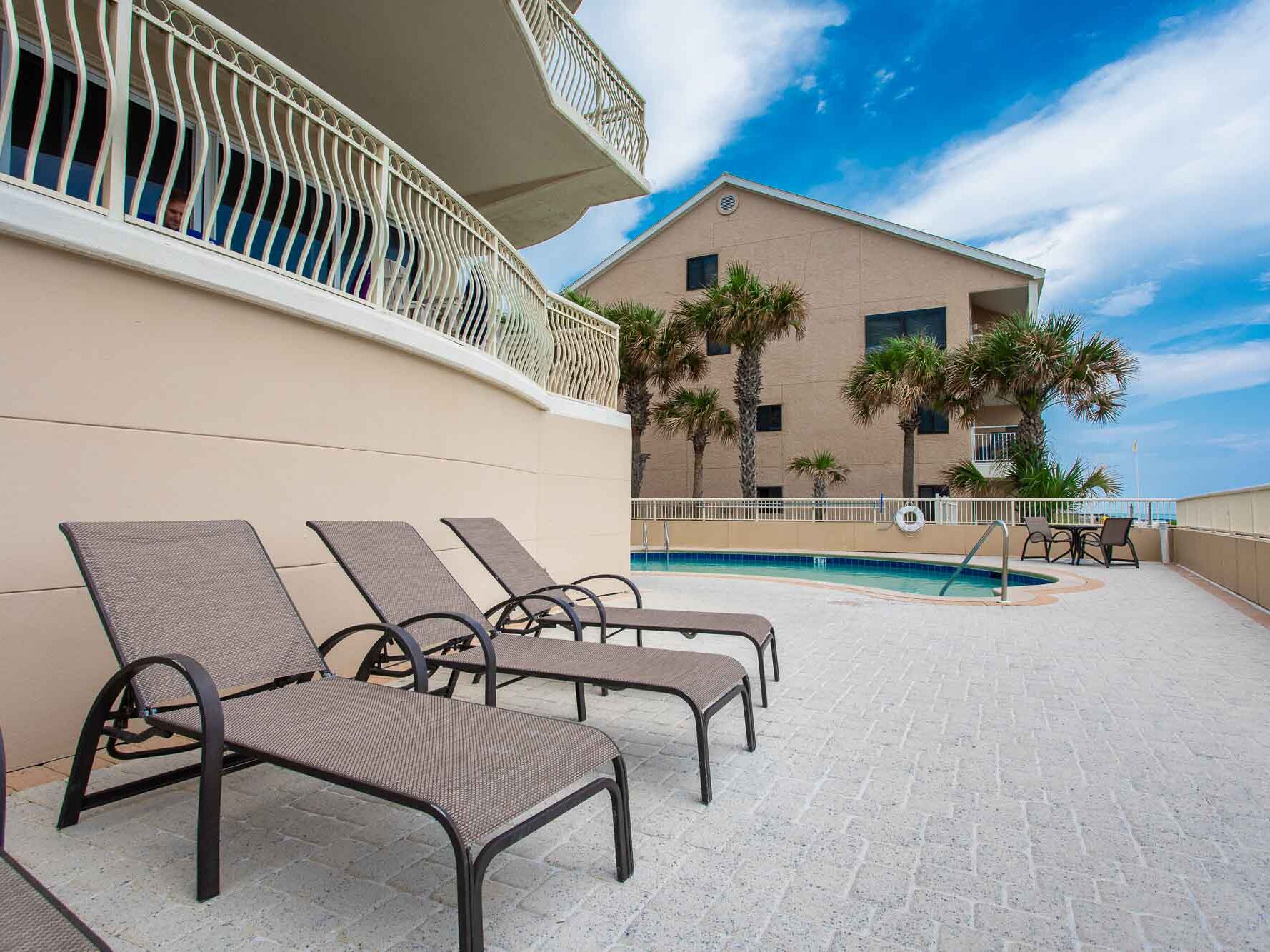 A poolside area with lounge chairs, a pool, and a building with a balcony.