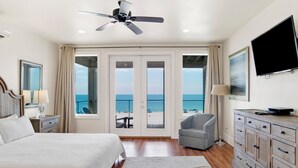 Een slaapkamer met een bed, een stoel, een dressoir, een televisie en een balkon met uitzicht op zee.