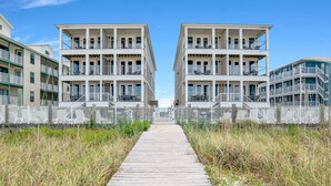 Een houten looppad dat naar een gebouw aan het strand leidt, met meerdere balkons en een witte hek.
