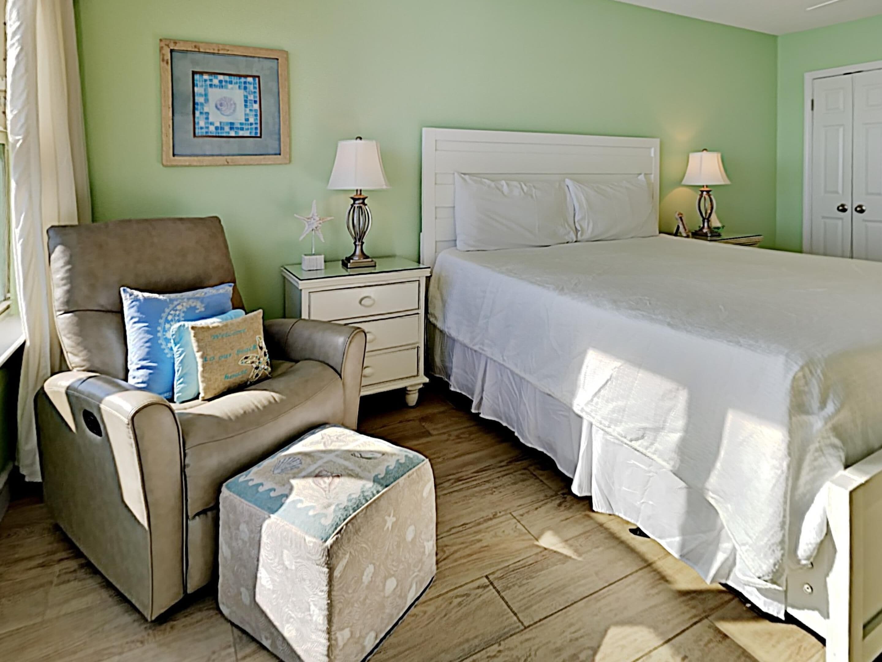 A bedroom with a bed, a chair, a nightstand, a lamp, and a framed picture on the wall.