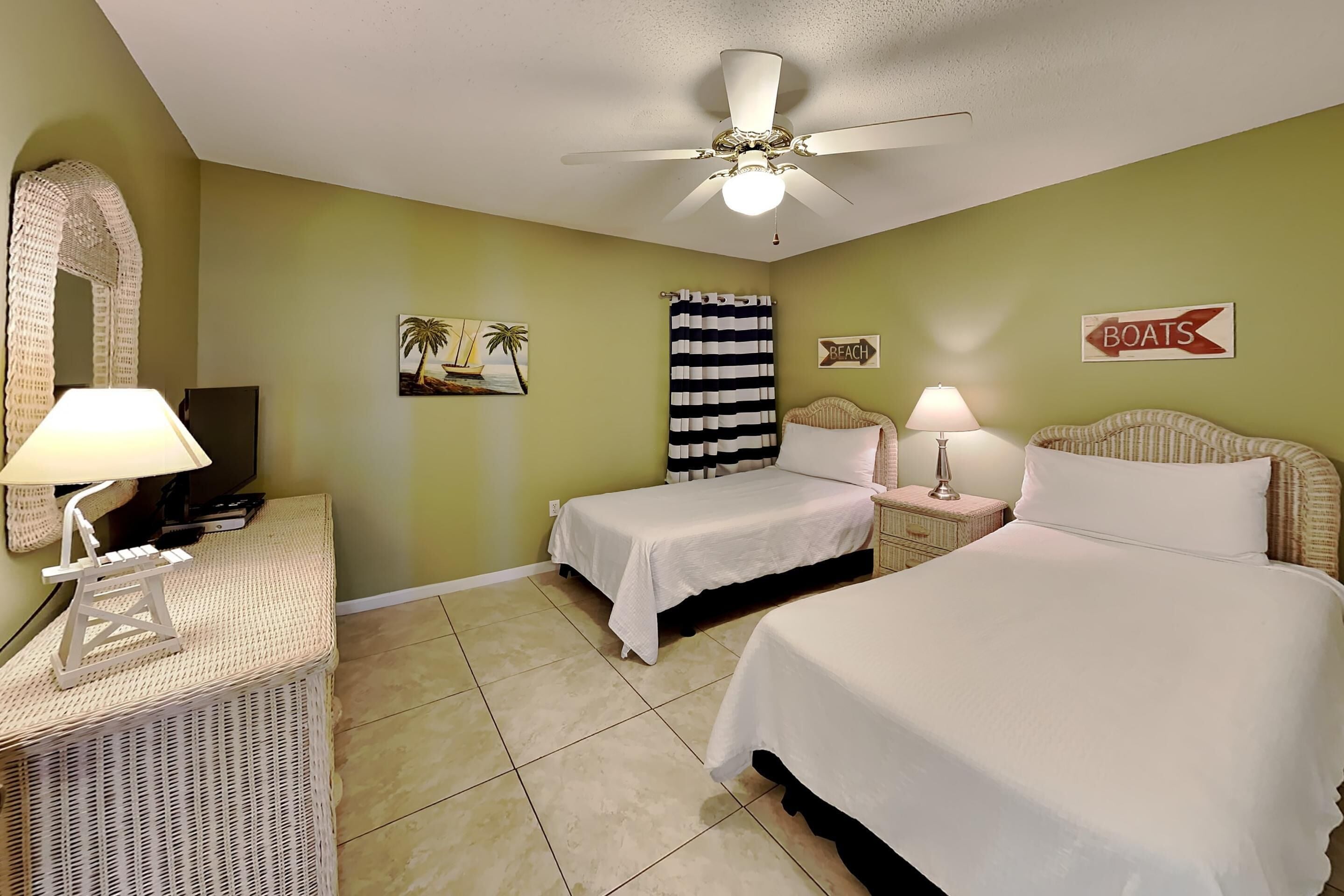 A room with two beds, a ceiling fan, a TV, and a sign that says "BOATS".