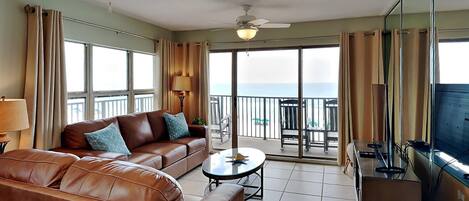 A spacious living room with a brown leather sofa, a round coffee table, and a balcony with a view of the sea.