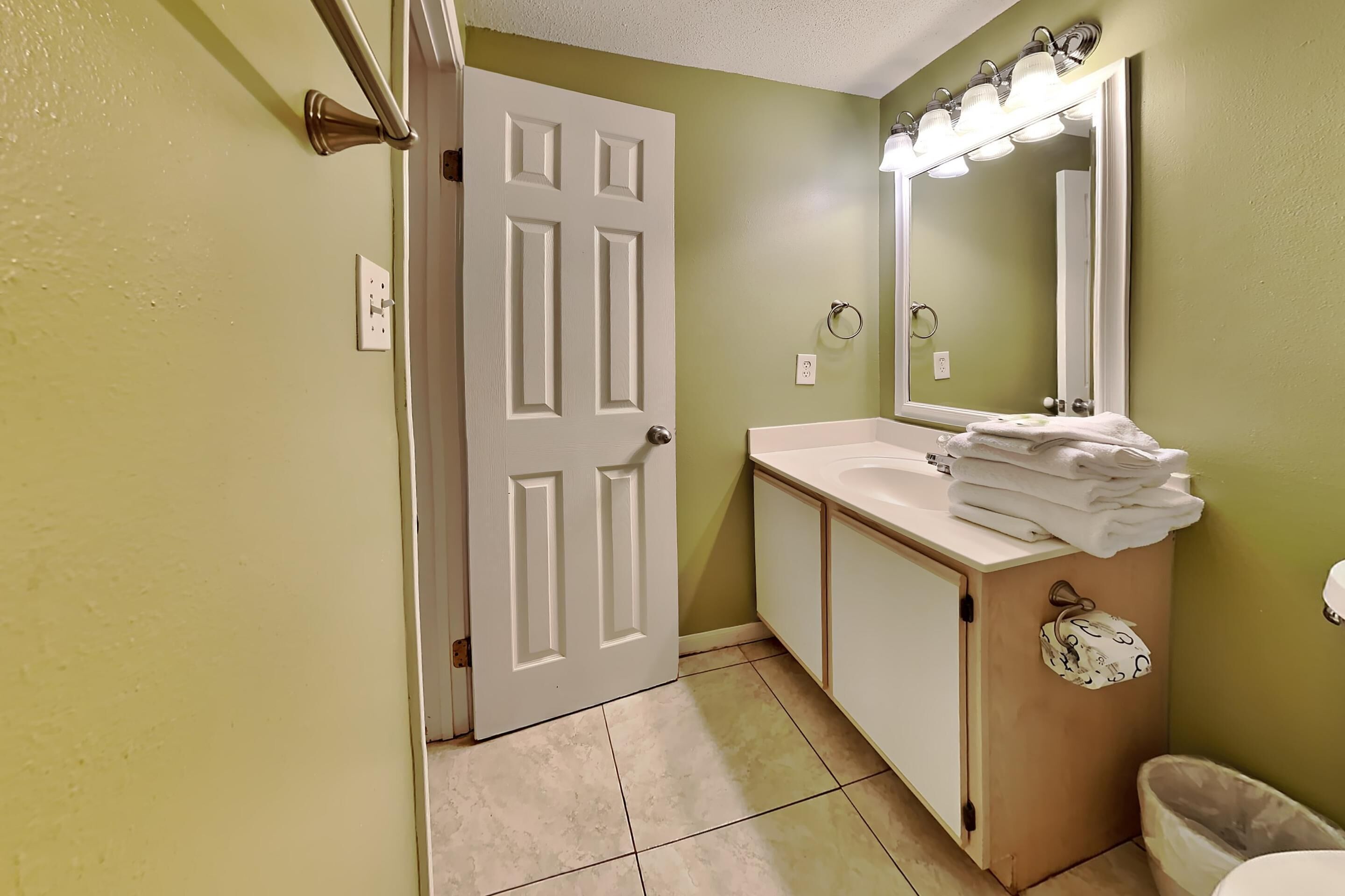 A bathroom with a white door, a sink with a mirror, and a towel rack.