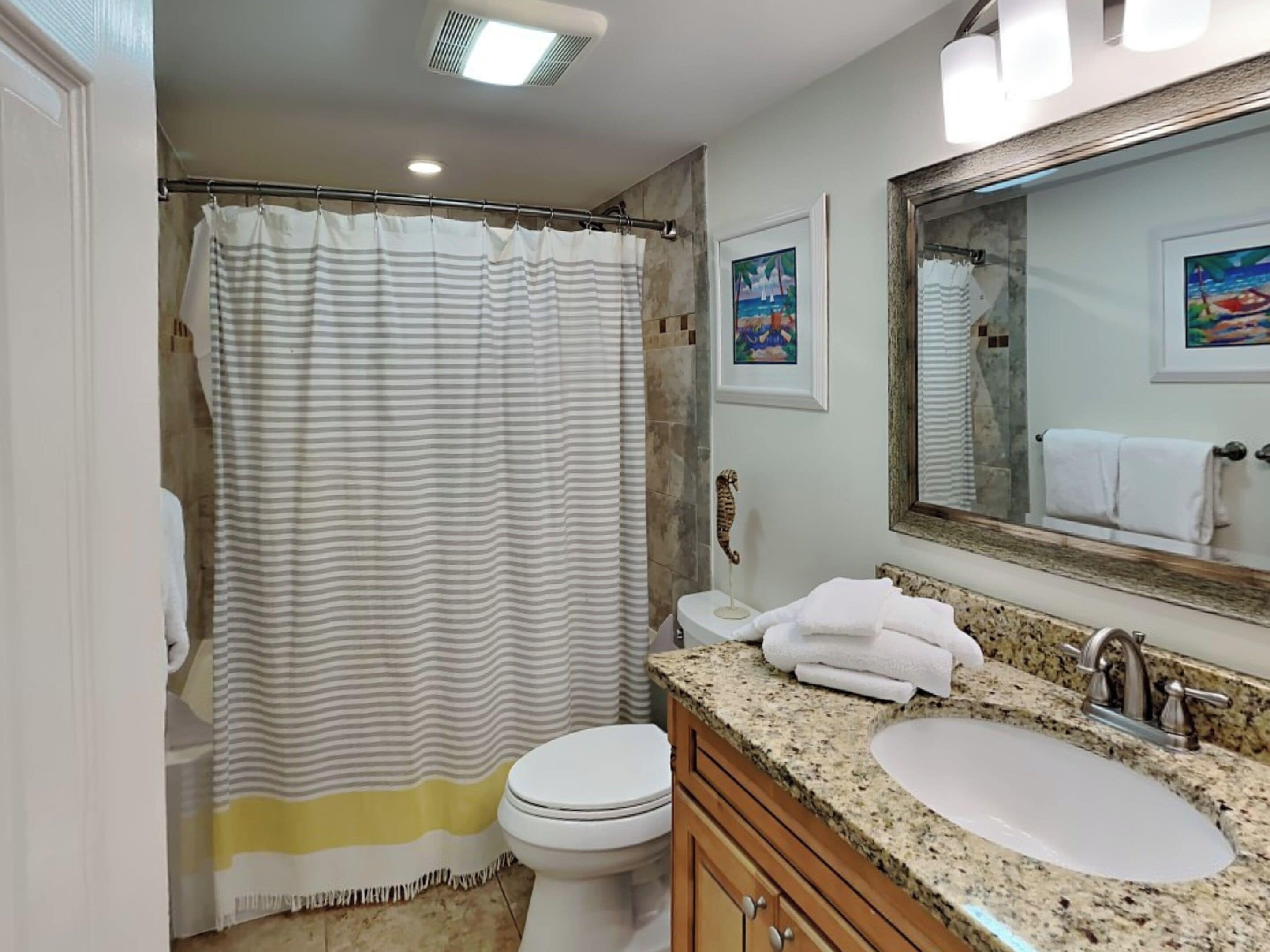 A bathroom with a striped shower curtain, a toilet, a sink with a mirror, and a towel rack.