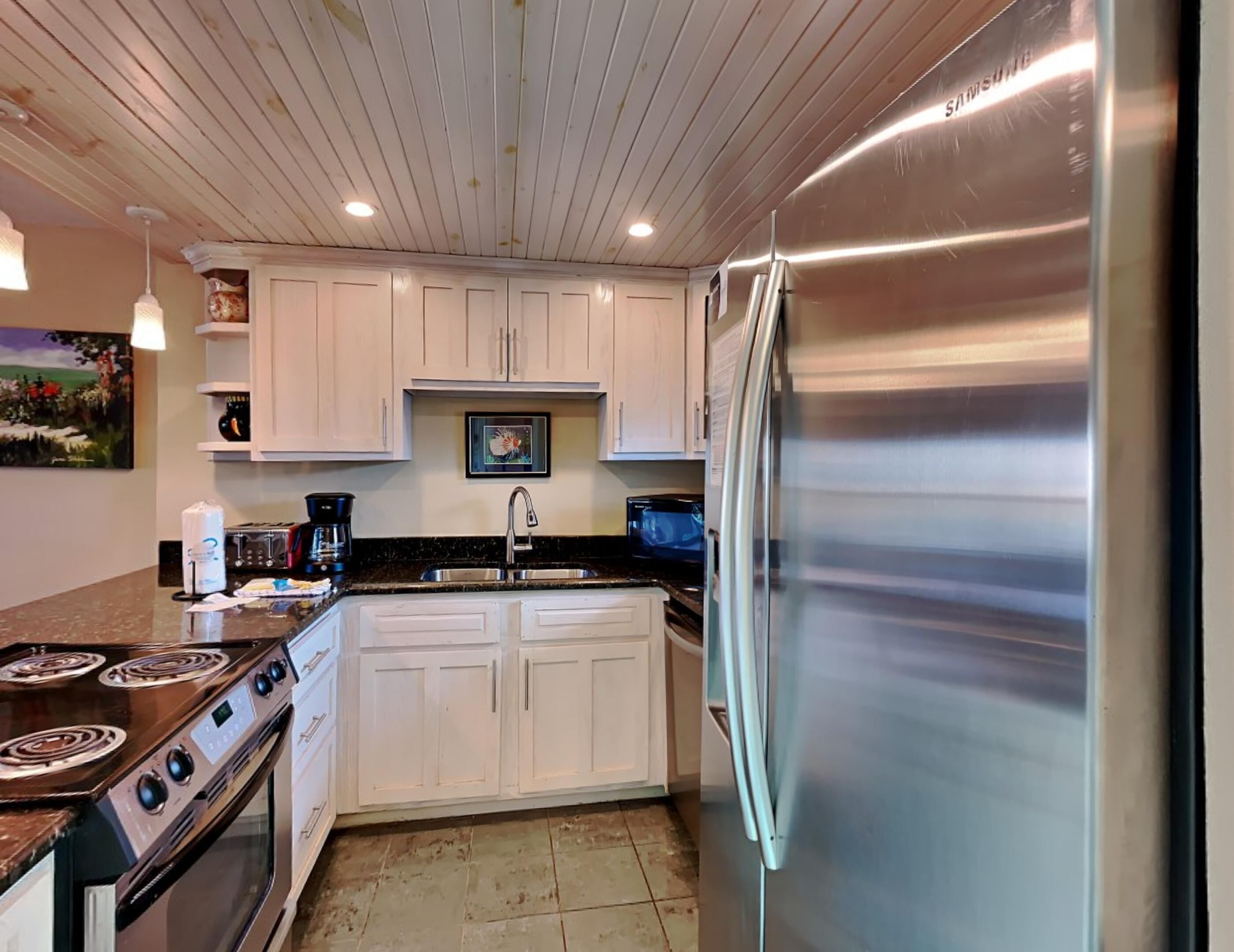 Una cocina con armarios blancos, electrodomésticos de acero inoxidable, una estufa a gas y un refrigerador.