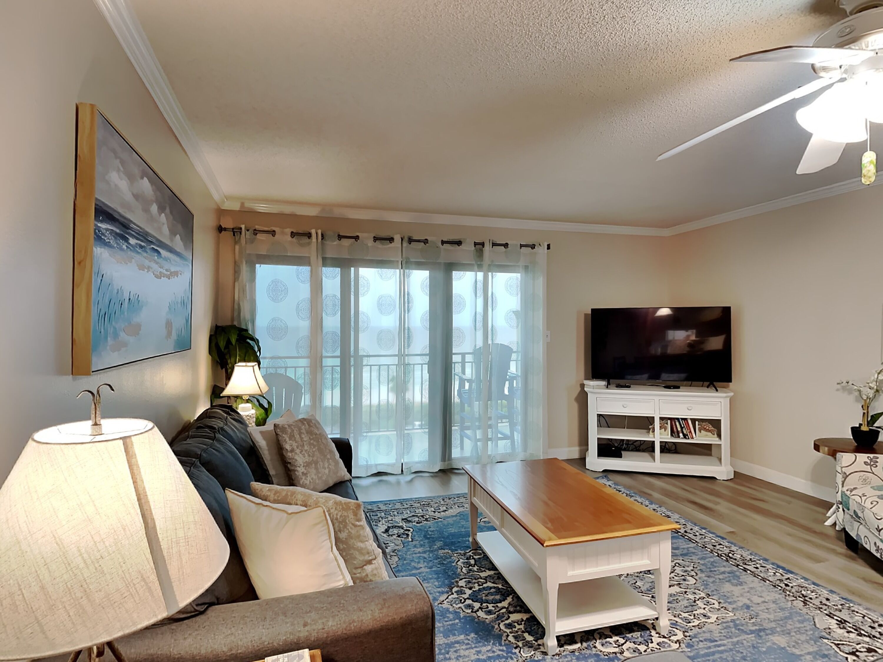 Una sala de estar con sofá, mesa de centro, televisor y un balcón con vistas.