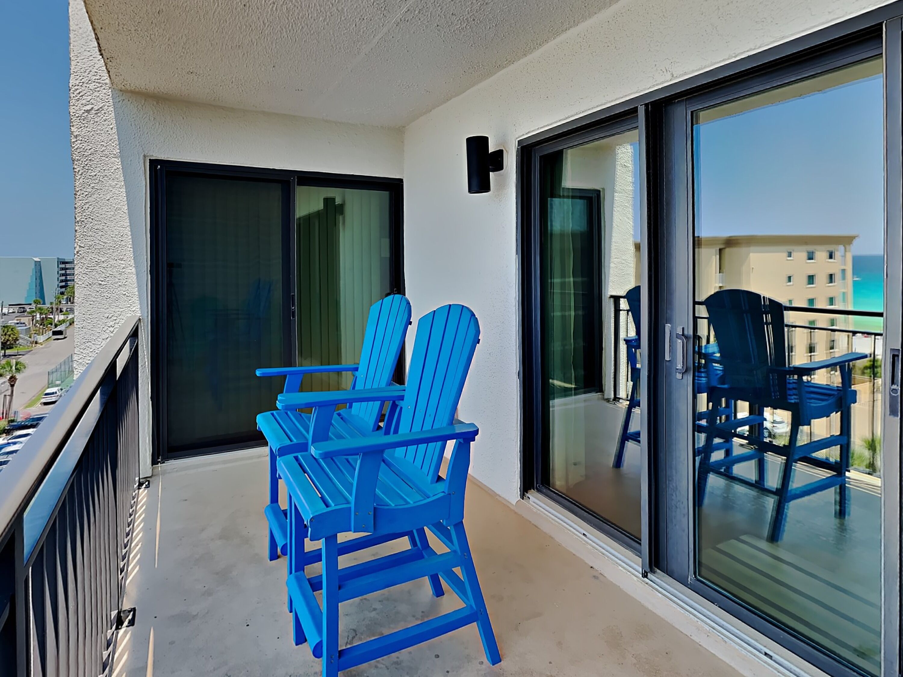 A balcony with blue chairs and a glass door leading to a pool area.