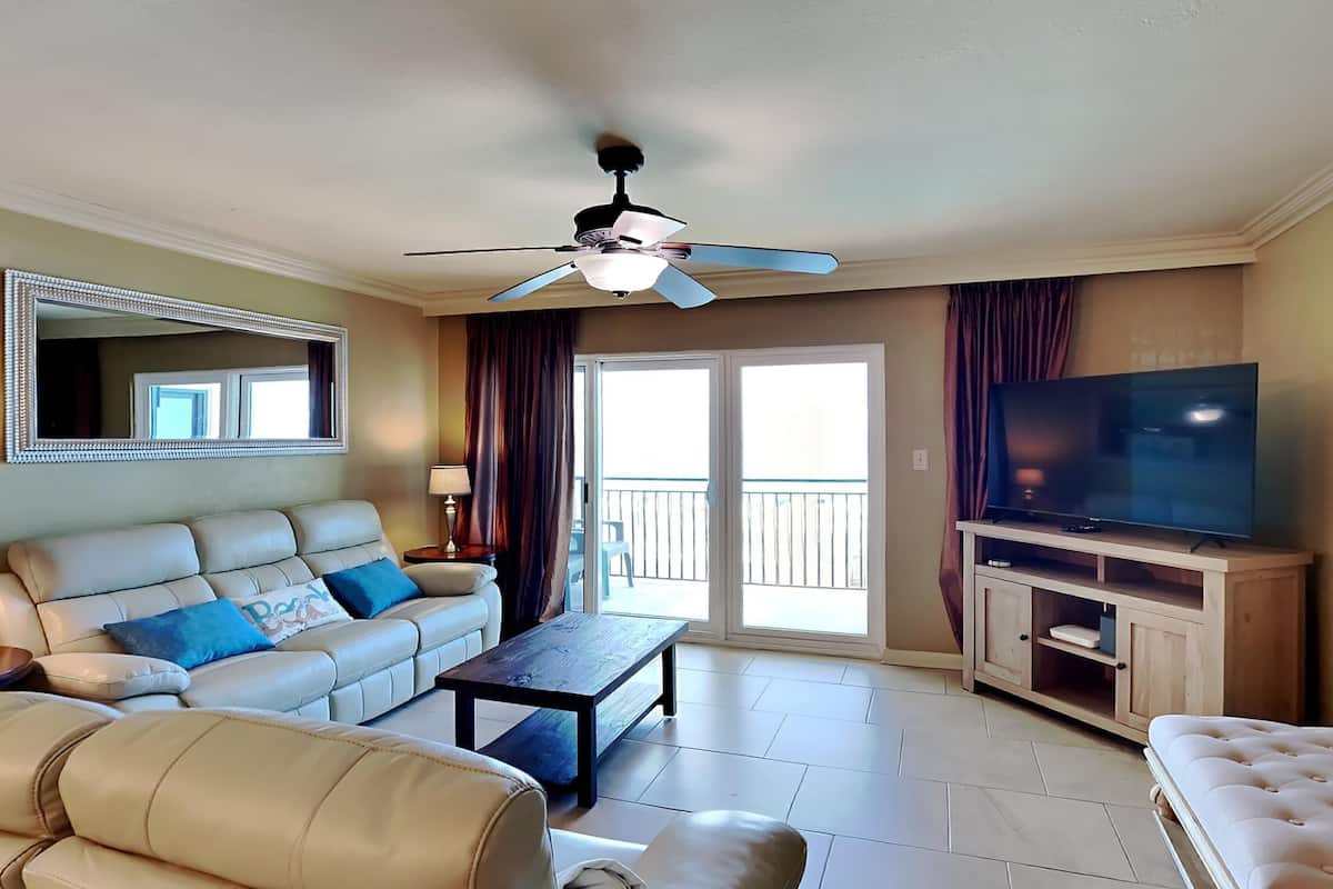 A living room with a sofa, a coffee table, a television, and a ceiling fan.