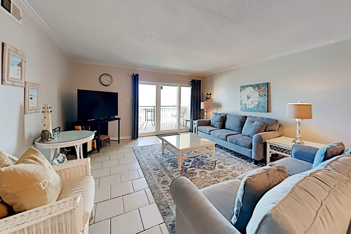 A living room with a sofa, a television, a coffee table, and a balcony with a view.