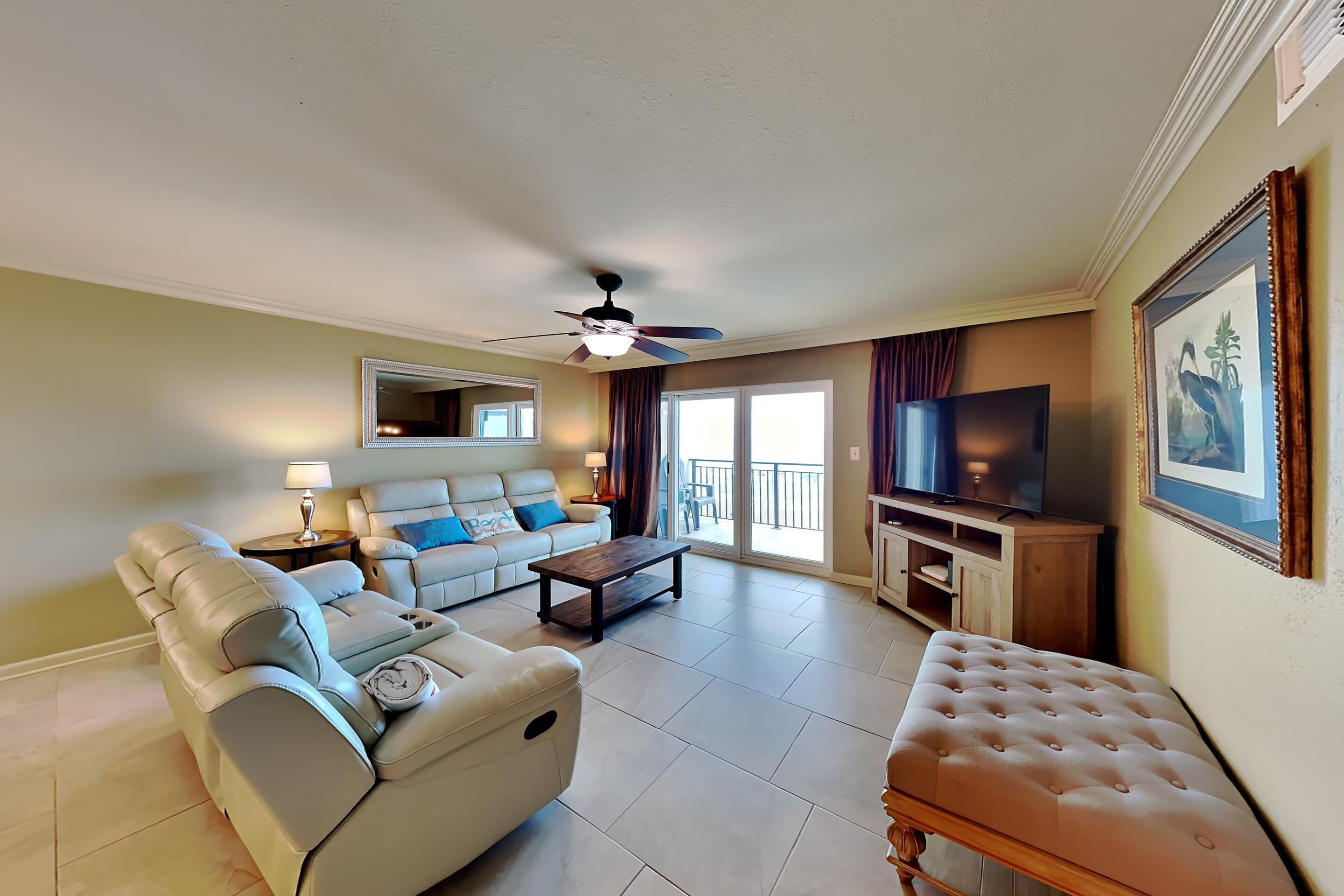 A living room with a sofa, a recliner, a coffee table, a TV, and a balcony with curtains.