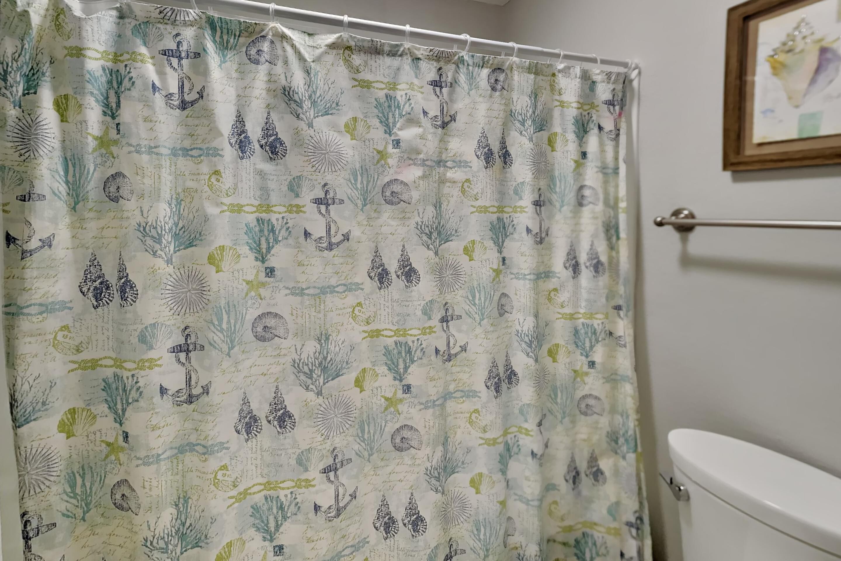 A bathroom with a shower curtain featuring a nautical theme, a toilet, and a framed picture on the wall.