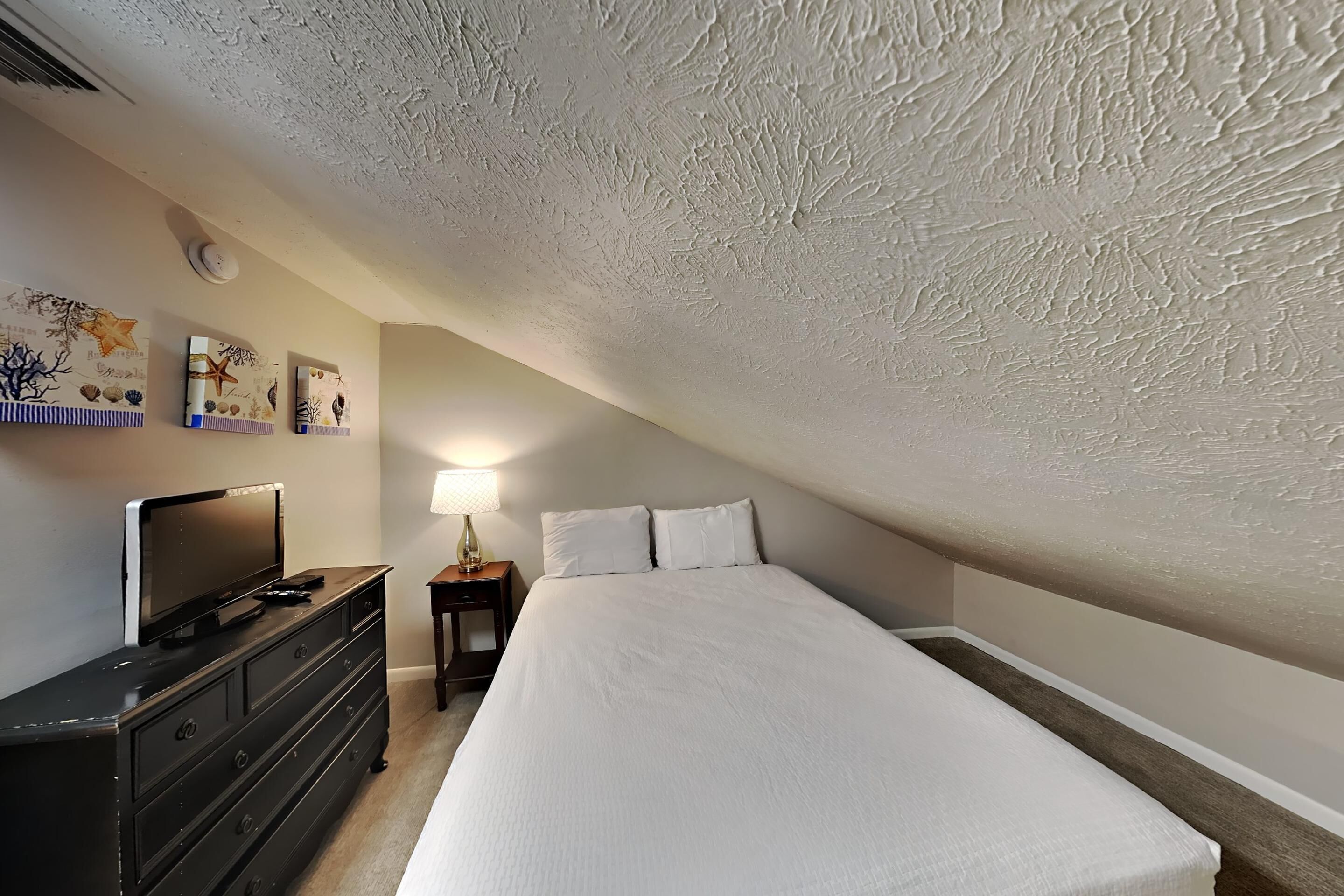 A bedroom with a bed, a dresser, a television, and wall art.