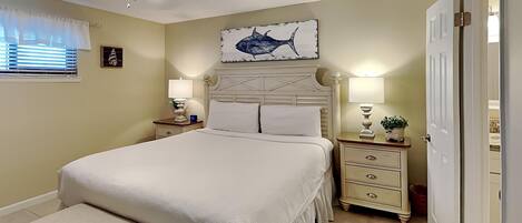 A bedroom with a bed, a bench, a ceiling fan, a wall-mounted artwork, and a door.