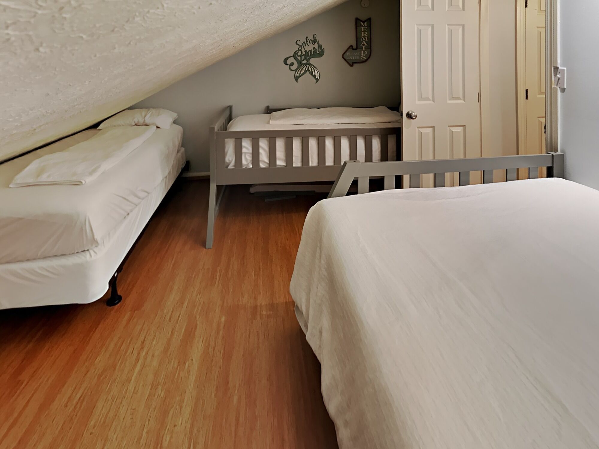 Een slaapkamer met twee eenpersoonsbedden, een houten vloer en een deur.