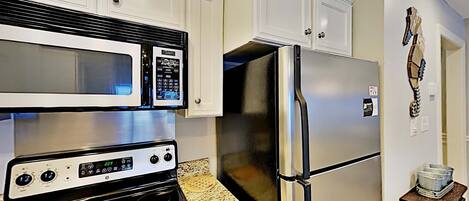 Una cocina con armarios blancos, un refrigerador de acero inoxidable, un microondas y un horno.