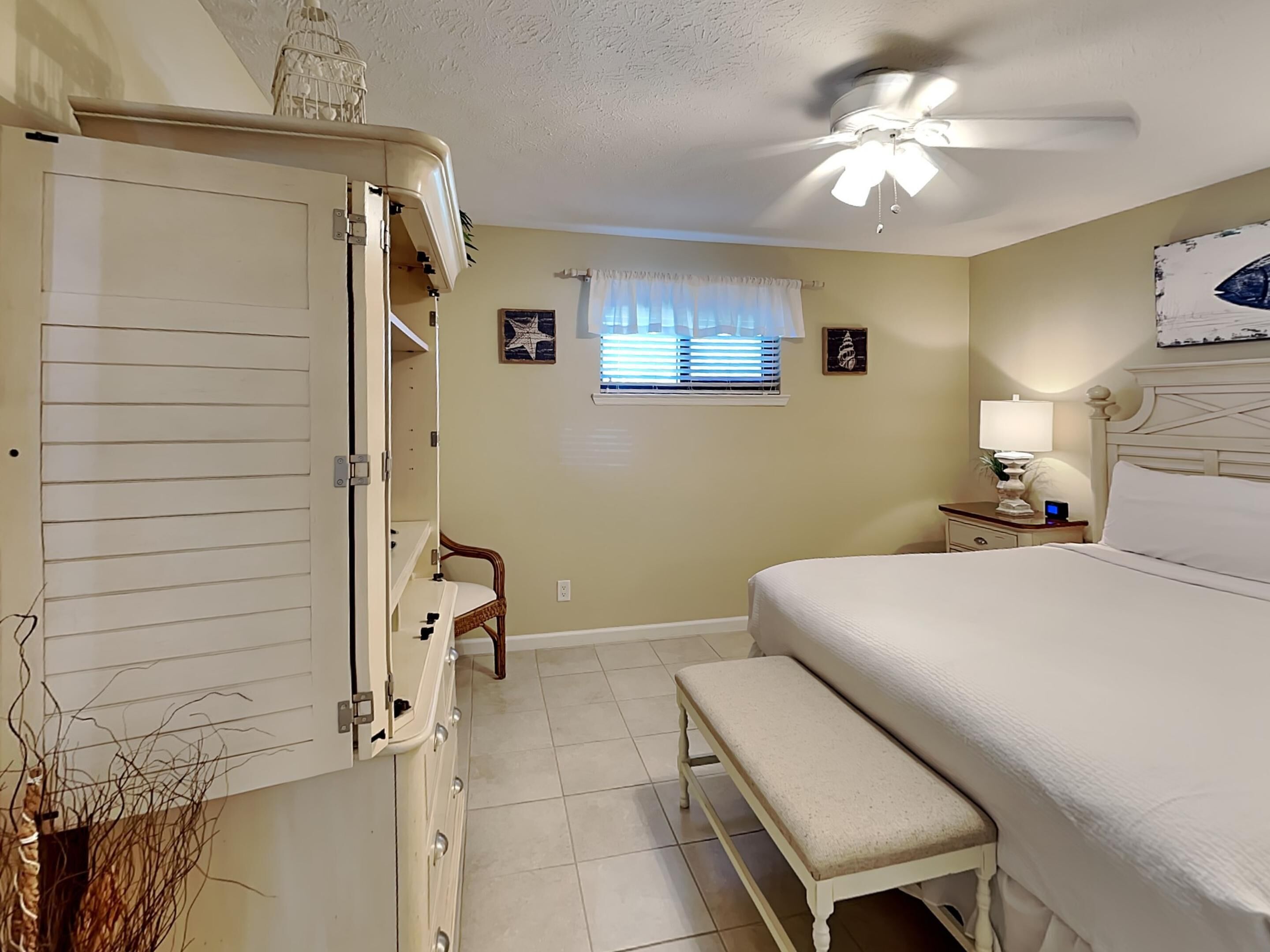 A bedroom with a bed, a bench, a nightstand, a ceiling fan, and a window with blinds.