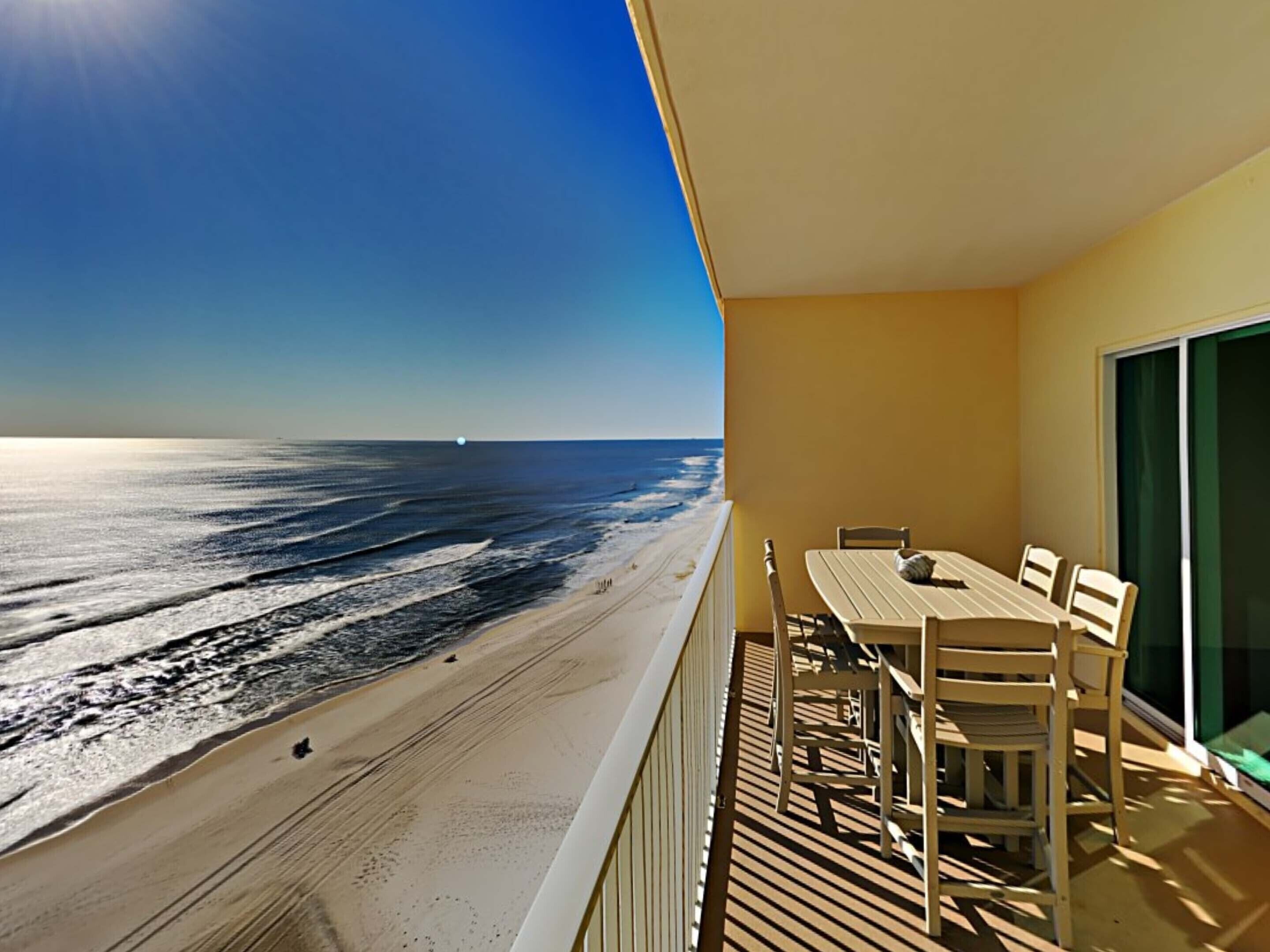 A balcony with a view of the ocean, a table, and chairs.