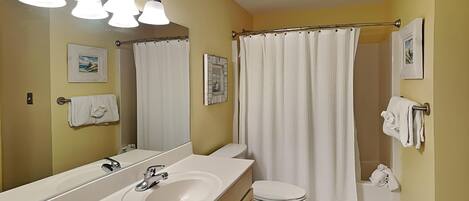 A bathroom with a large mirror, a sink, a toilet, a shower curtain, and towels on the wall.
