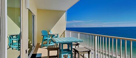A balcony with turquoise chairs and a table, overlooking a beach.