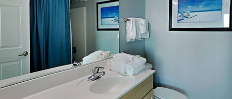A bathroom with a white sink, a mirror, a toilet, and a shower curtain.