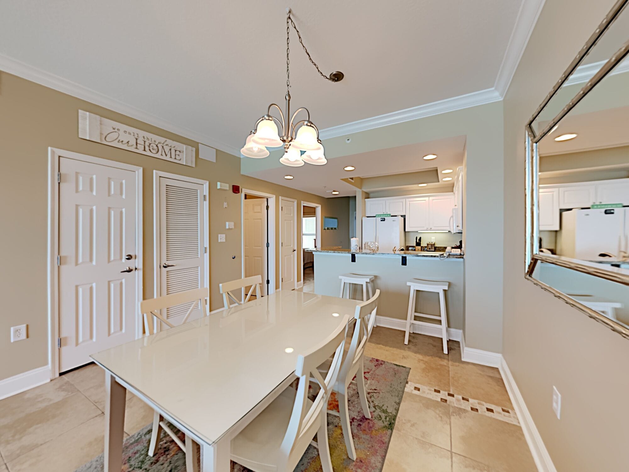 A spacious dining area with a large table and chairs, a chandelier, and a kitchen in the background.