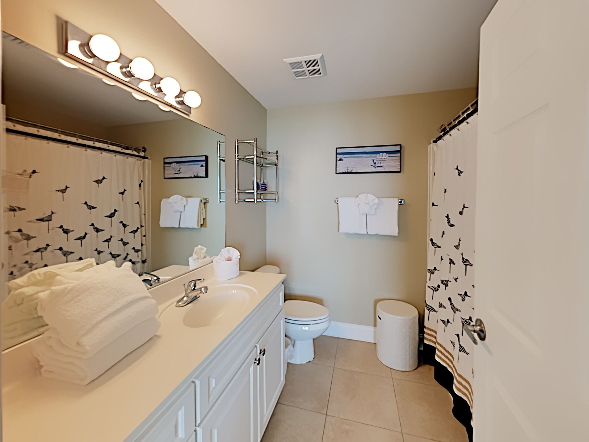 A bathroom with a sink, mirror, and toilet. There are towels and a trash can.