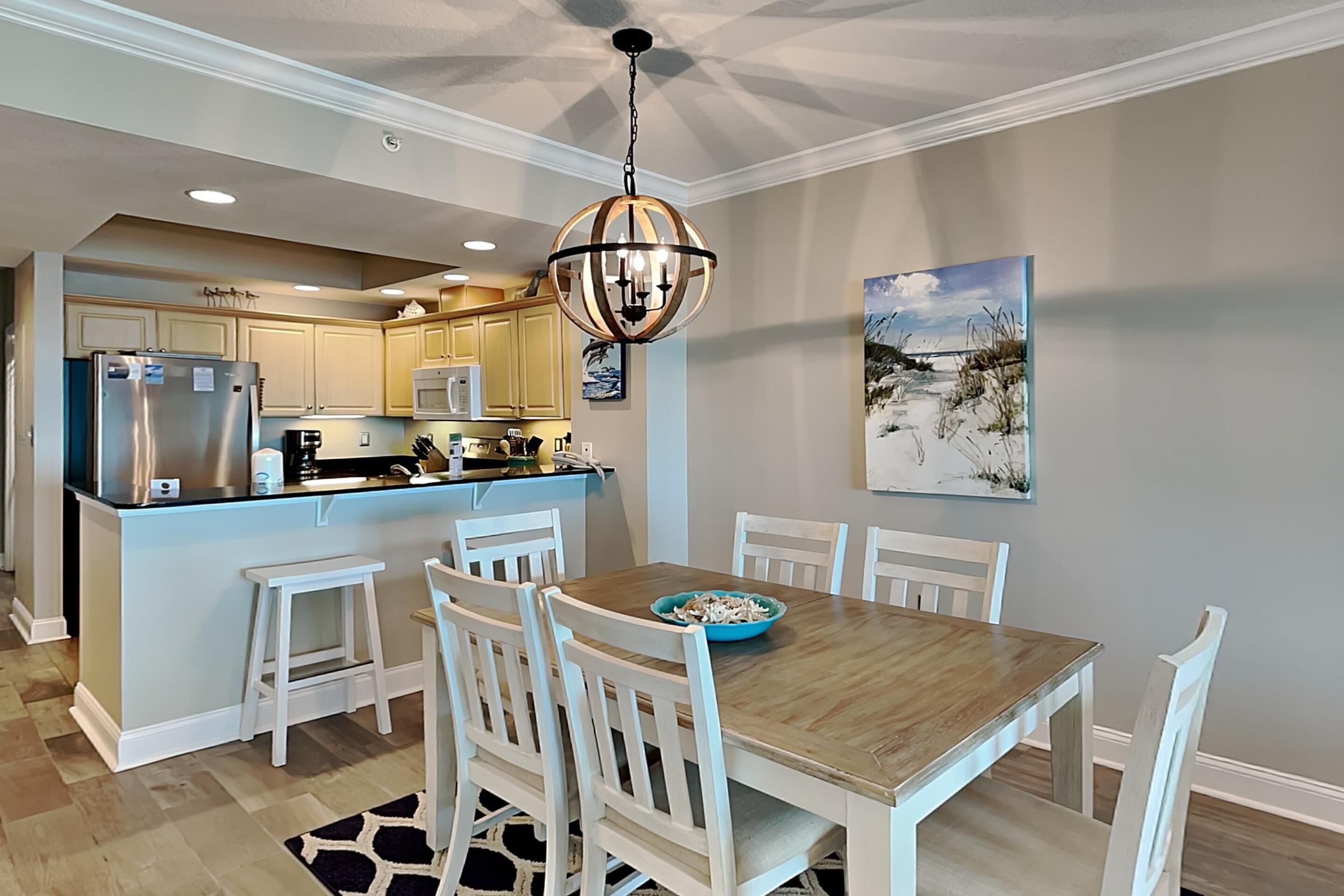 Une cuisine moderne avec des meubles blancs, un réfrigérateur en acier inoxydable et une table à manger en bois, assortie de chaises blanches.