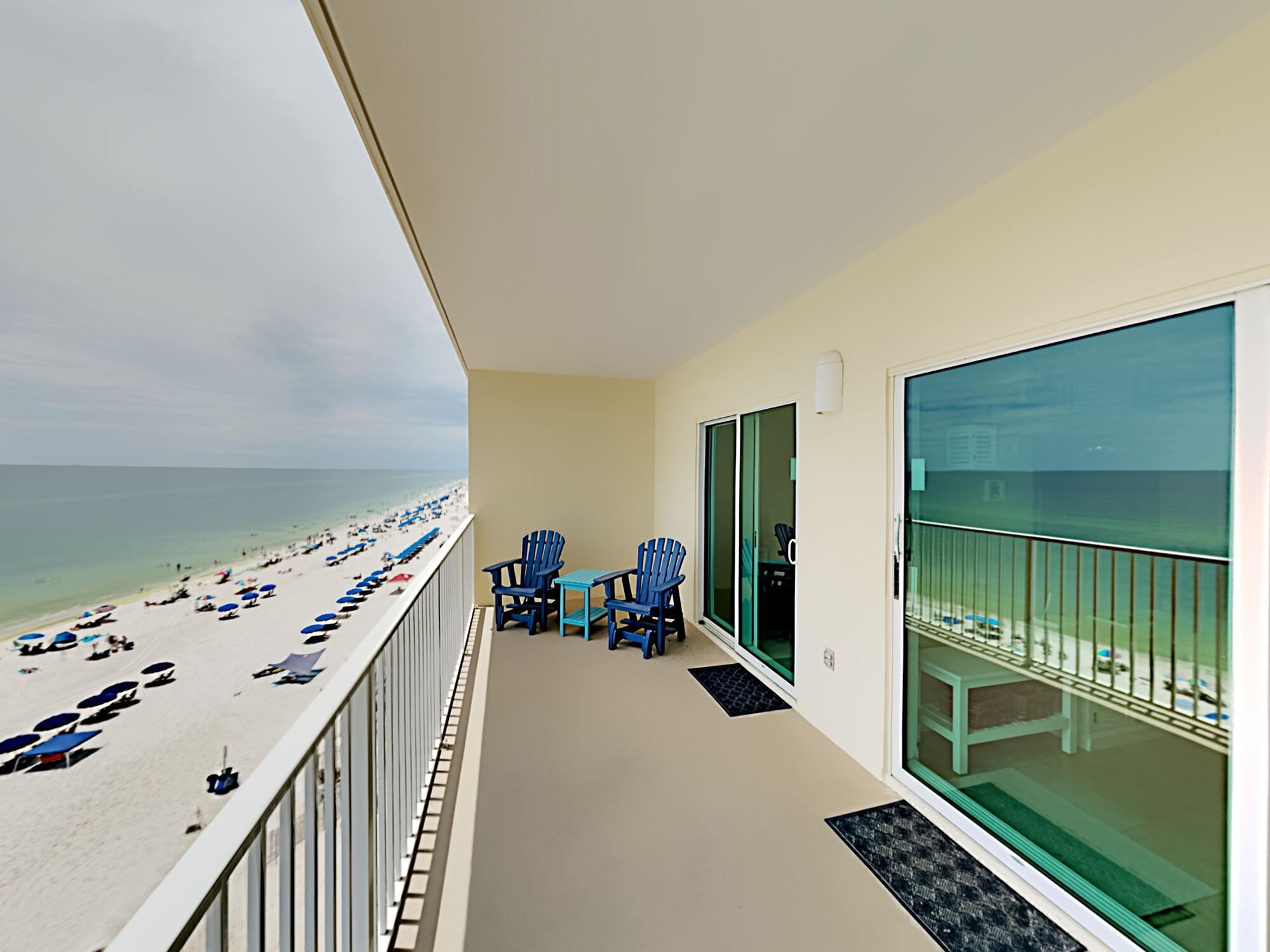 A balcony with a view of the beach, two blue chairs, and a small table.