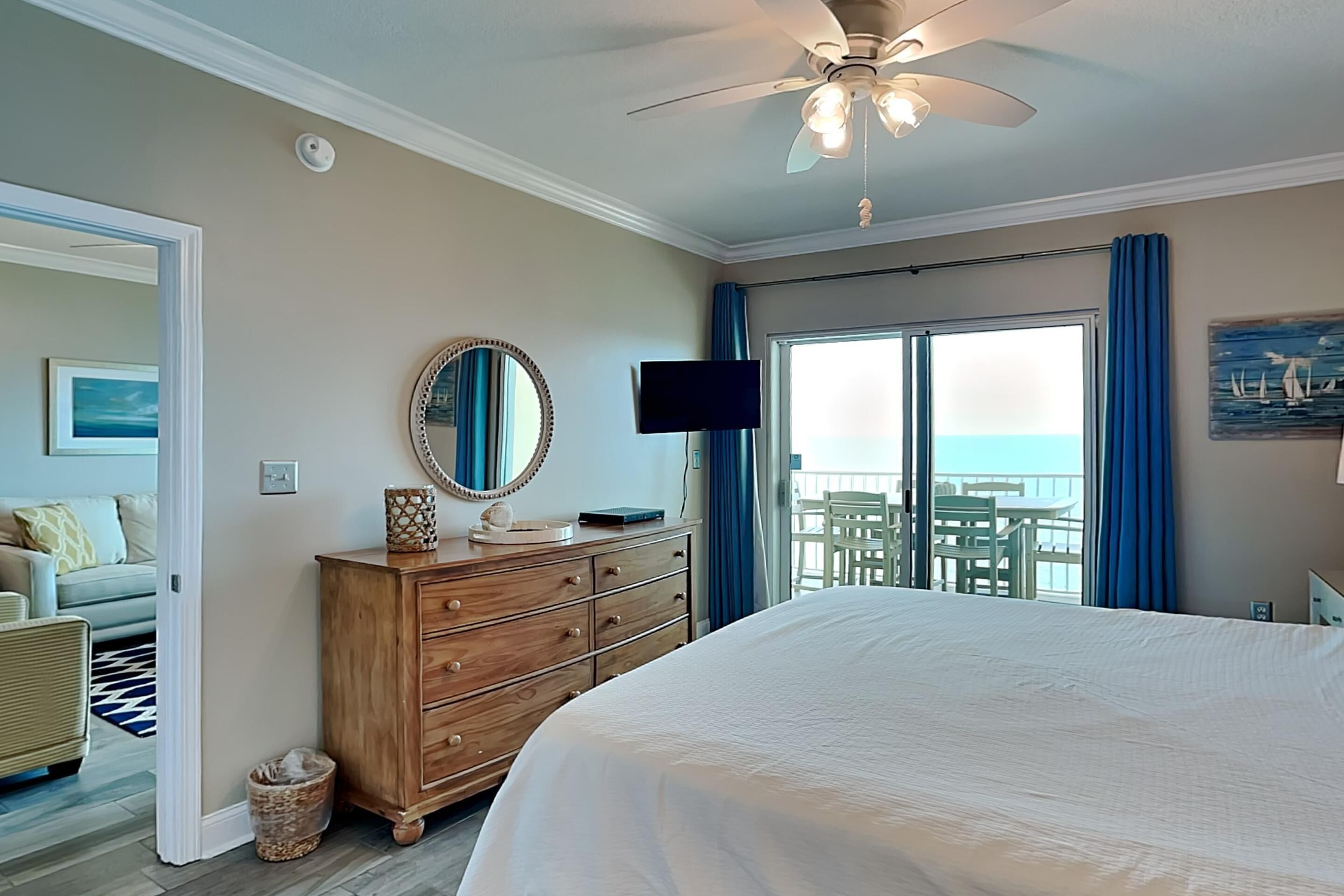 Une chambre dotée d’un grand lit, d’un ventilateur de plafond, d’une commode, d’une télévision et d’un balcon offrant une vue sur l’océan.