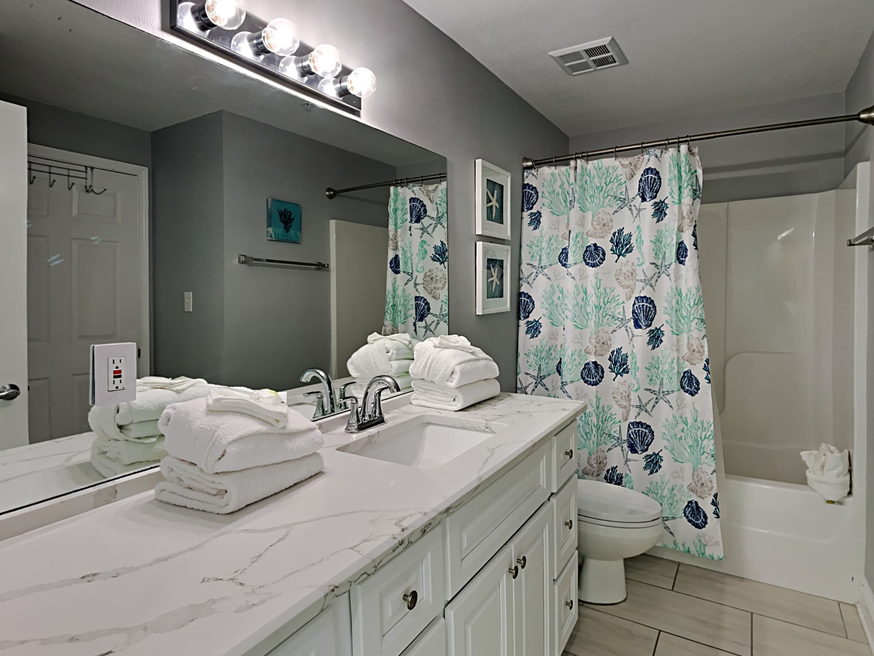 A bathroom with a white vanity, a sink, a mirror, and a shower curtain with a floral pattern.