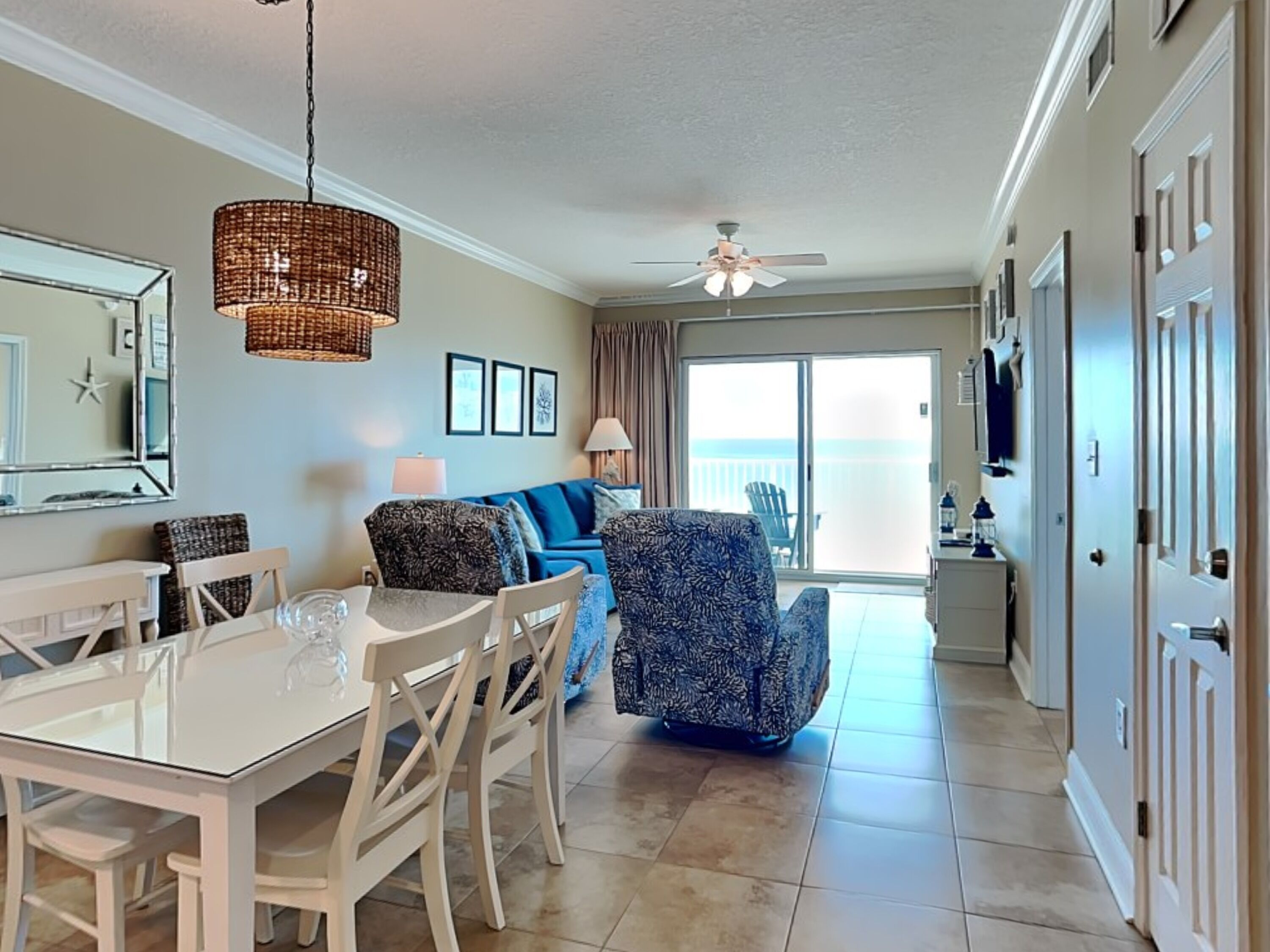 A spacious living area with a dining table, blue patterned sofa, and a balcony with a view.