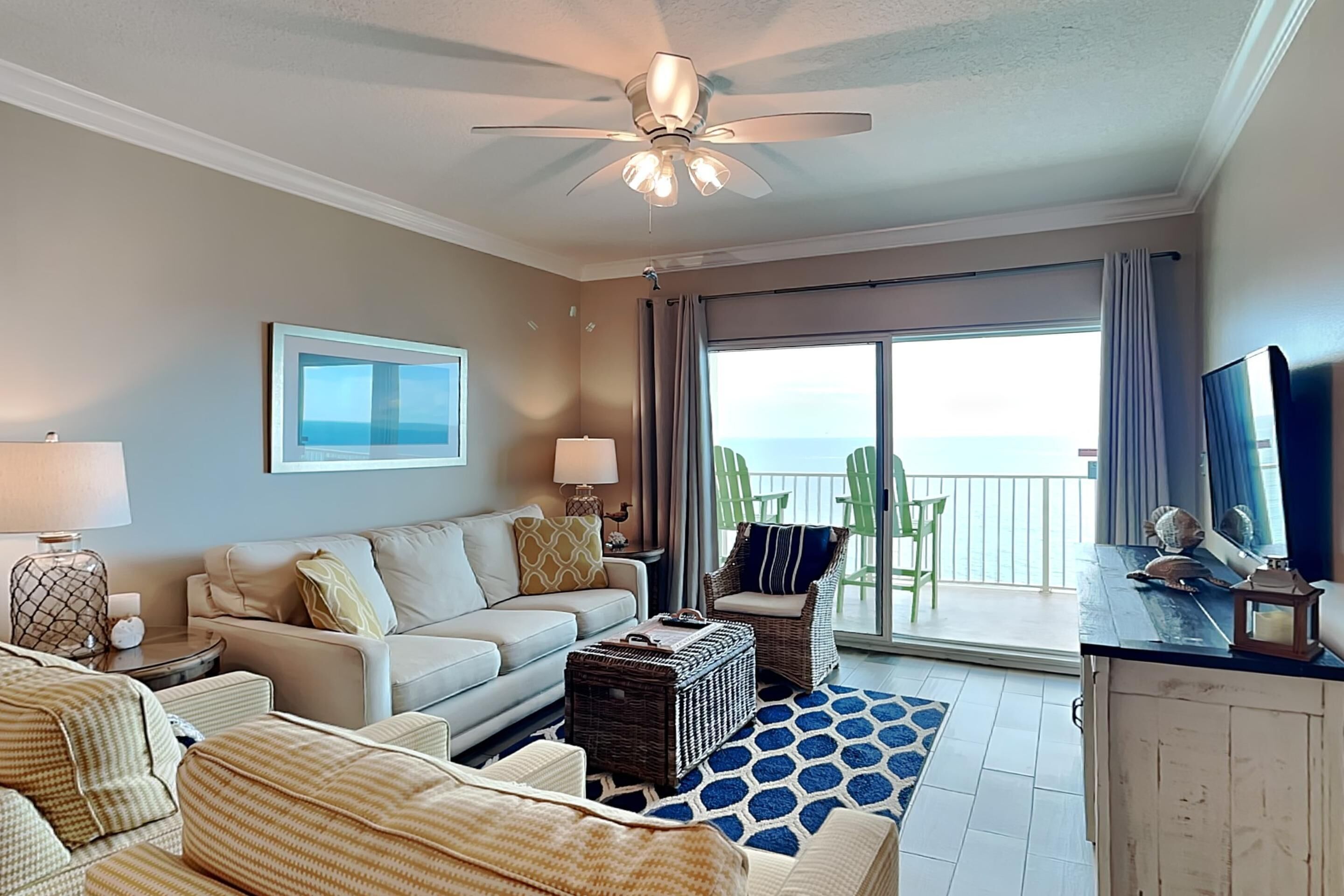 A spacious living room with a large window, a ceiling fan, and a view of the ocean.