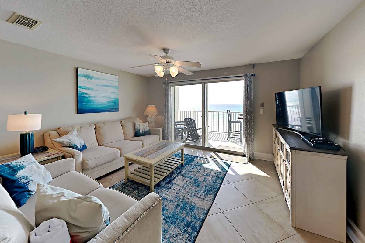 A living room with a sofa, coffee table, TV, and a balcony with a view.