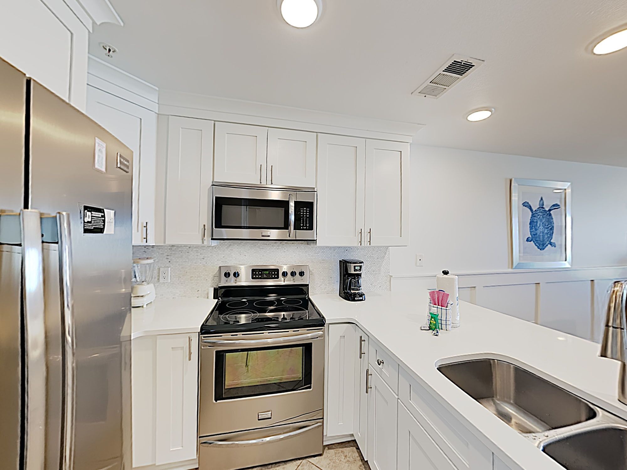 A modern kitchen with white cabinets, stainless steel appliances, a built-in oven, a microwave, and a coffee maker.