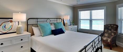 Ein Schlafzimmer mit einem Bett, Nachttischen, einem Sessel, einem Deckenventilator und einem Fenster mit Jalousien.