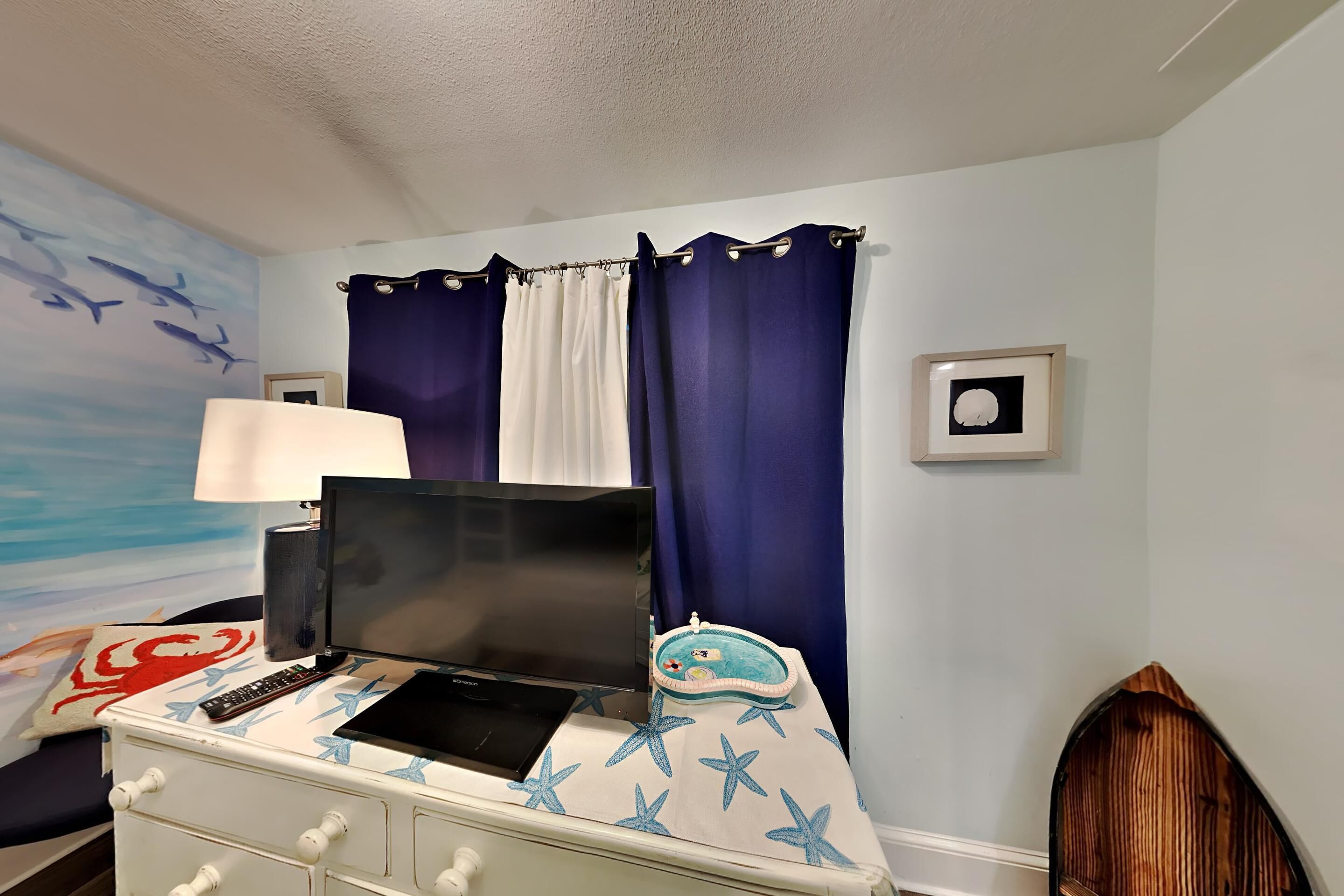 A bedroom with a bed, a desk with a laptop, a lamp, and curtains.