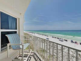 A balcony with a striped chair and a view of a beach with umbrellas and people.