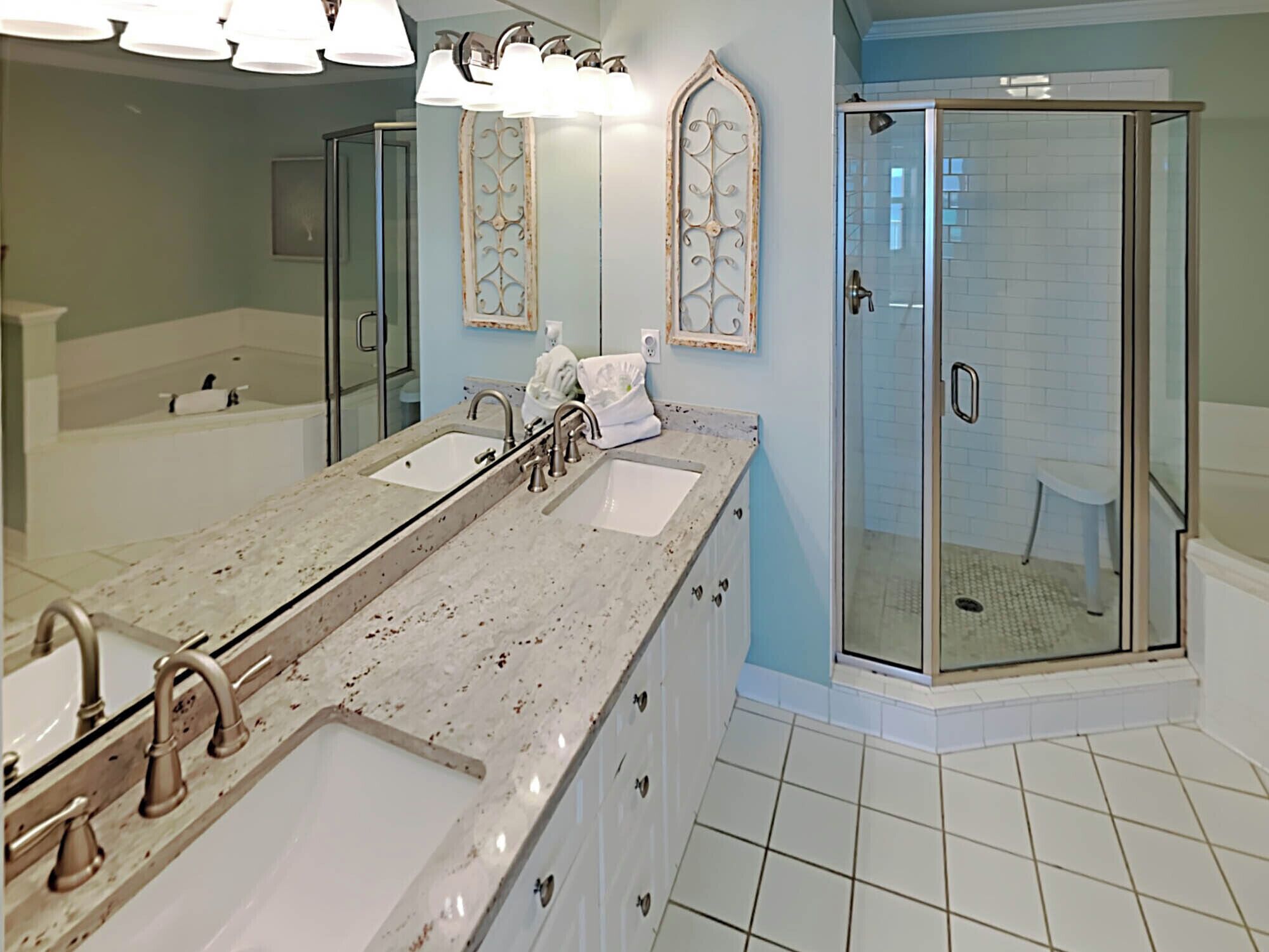 A modern bathroom with a large vanity, two sinks, a shower with glass doors, and decorative wall sconces.
