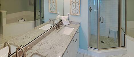 A modern bathroom with a large vanity, two sinks, a shower with glass doors, and decorative wall sconces.