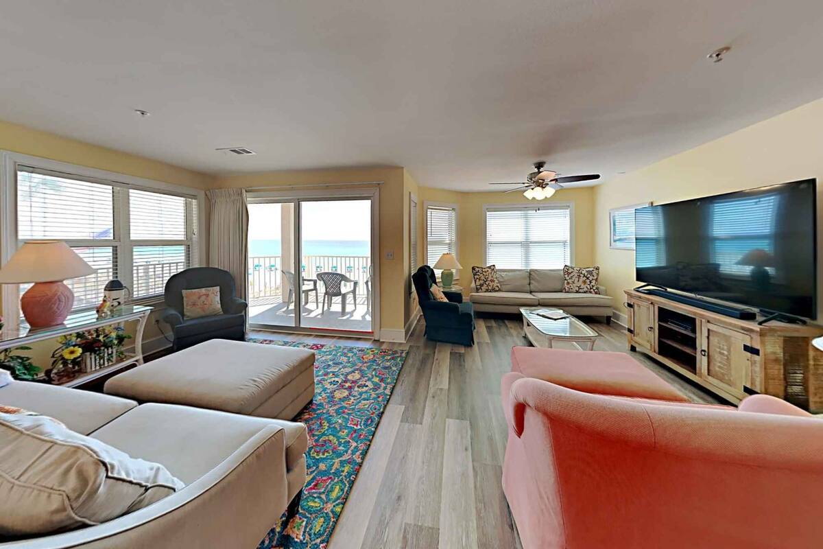 A living room with a sofa, armchairs, a coffee table, a TV, and a balcony with a view.