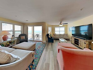 A living room with a sofa, armchairs, a coffee table, a TV, and a balcony with a view.