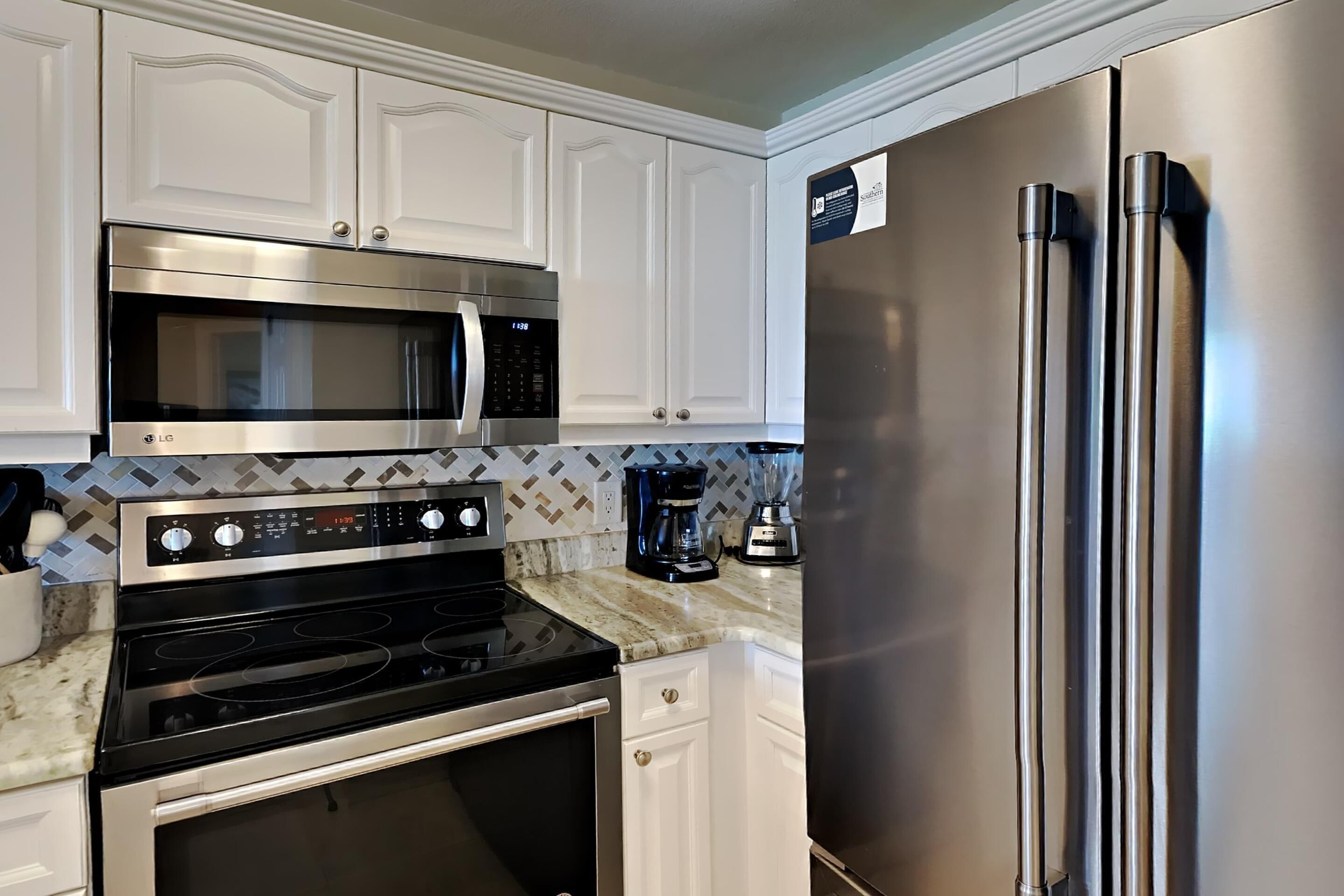 A kitchen with white cabinetry, a stainless steel microwave, a black stove, and a stainless steel refrigerator.
