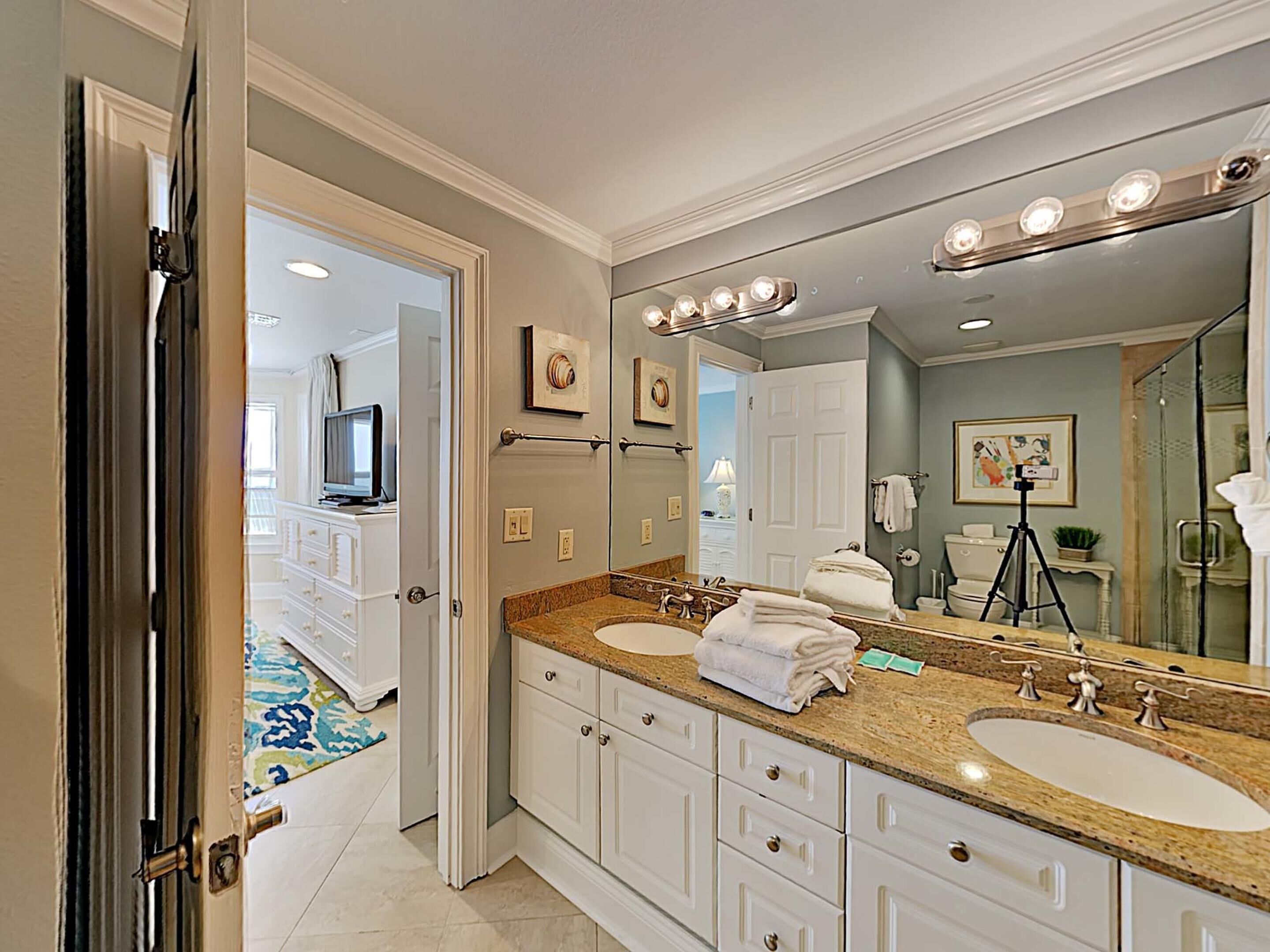 Une salle de bain avec deux lavabos, un grand miroir avec éclairage, un meuble-lavabo et une porte donnant sur une autre pièce.