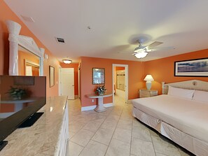 A hotel room with a bed, a desk, a chair, a ceiling fan, a bathroom, and a shower.